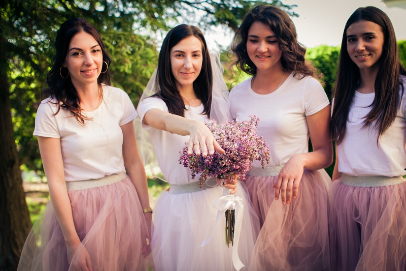Mismatched Dresses with Coordinated Themes The beautiful bride is standing with girlfriends on the outdoors and shows a wedding ring