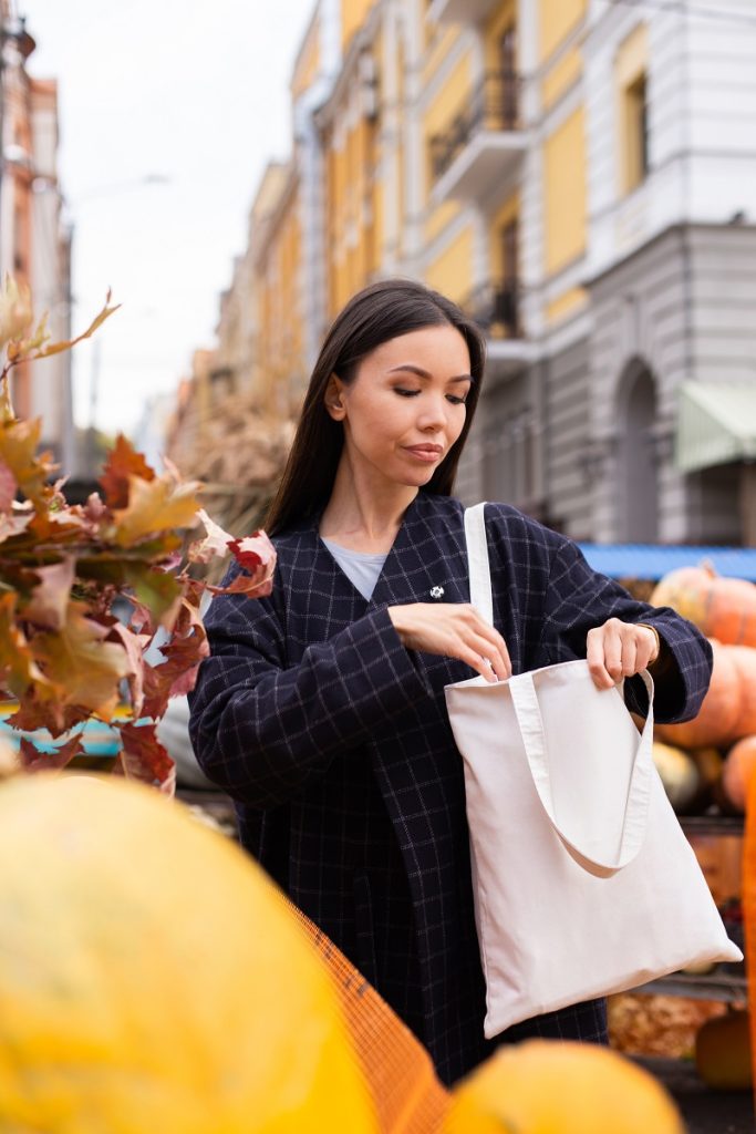 Tote Bags: Functional Glamour Portrait of young attractive casual woman looking for purse in bag at autumn farm shop outdoor